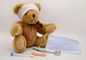 pictured: a teddy bear wears a bandage and sits beside medical implements 