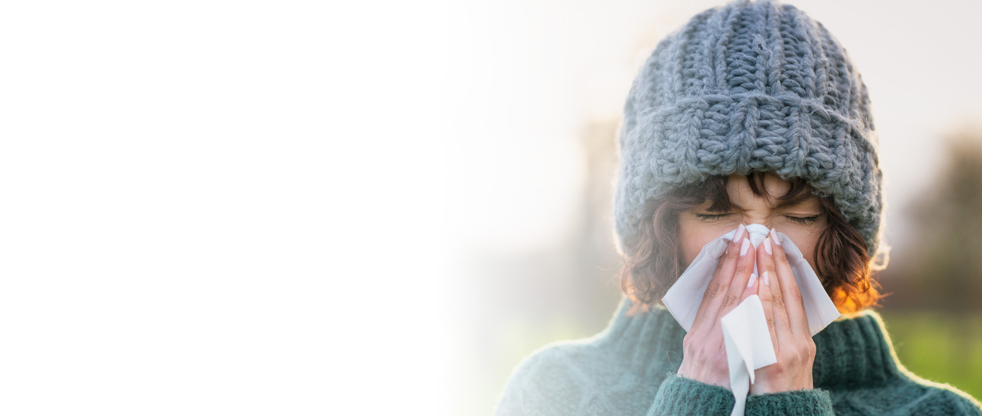 pictured: a woman wearing a knit beanie cap blows her nose